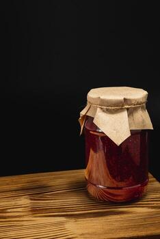 Homemade raspberry and cherry jam in a large jar on a wooden surface photo