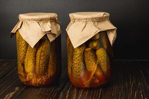 Homemade canned pickles and tomatoes in jars on wooden table photo