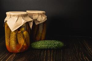 Homemade pickled cucumbers and tomatoes in jars on a wooden table photo