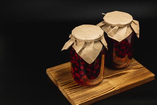 Homemade cherry and raspberry jam in large jars on a wooden board photo