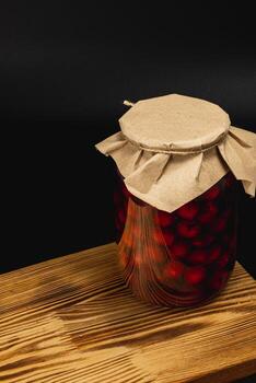 Homemade cherry and raspberry jam in large jar on wooden table photo