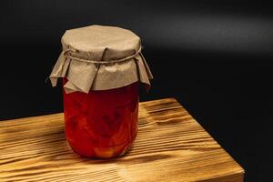 Homemade pickled tomatoes in jar on wooden board ready for storage photo
