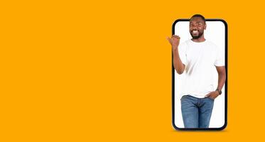 A man stands inside a smartphone, smiling and gesturing with his hand, showcasing effective communication. The vibrant yellow background adds a lively touch to the interaction. photo