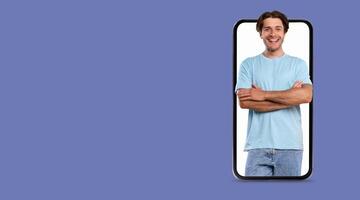 A person stands with arms crossed, smiling at a large smartphone screen. The background is a solid color, emphasizing the modern technology and social communication. photo
