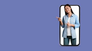 A joyful woman stands in front of a large smartphone display, interacting with a social media application. She points enthusiastically, highlighting modern communication technology. photo