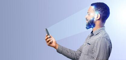 A man stands in an isolated setting, using facial recognition technology on his smartphone. He gazes at the screen, highlighting advancements in identification and security. photo