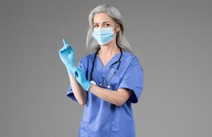 A middle aged woman in scrubs wears a mask and gloves while preparing for a medical examination. She appears focused and ready to provide healthcare in a clinical setting. photo