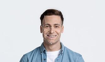 Smiling young man is featured against a plain background, demonstrating facial recognition technology with geometric lines outlining his face, emphasizing identification capabilities. photo