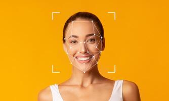 A smiling woman stands in front of a bright yellow background, demonstrating facial recognition technology. The facial features are highlighted with geometric patterns, indicating ID capabilities. photo