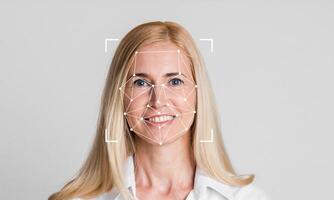 A woman smiling with facial recognition technology overlay on her face. The background is plain and light, emphasizing the subject's features and the tech aspect of identification. photo