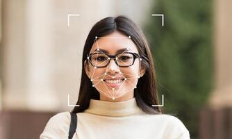 A woman is smiling at the camera while facial identification technology tracks her features. The background features soft greenery, suggesting an outdoor location. photo