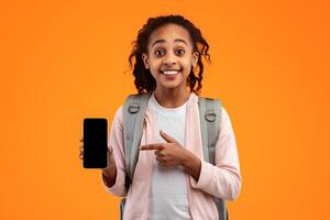 Mobile Application Ad. Portrait Of Excited African Girl Showing Phone Empty Screen Recommending App Standing Over Yellow Studio Background, Smiling To Camera. Cellphone Display Mockup, Check This Apps photo