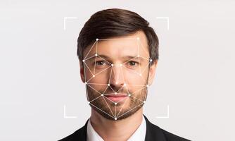 A man in formal attire is positioned against a neutral background, with facial recognition markers overlaid on his face. The technology highlights individual identification capabilities. photo