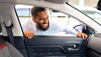 Smiling Black Man Choosing New Vehicle, Looking Inside Of Car With Excitement, Happy Male Buyer Checking Interior And Auto Characteristics While Spending Time In Dealership Center, Closeup photo