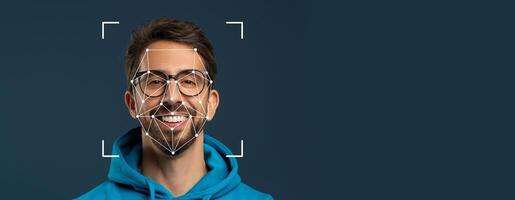 A smiling man wears glasses and a hoodie while facial recognition technology overlays a geometric pattern on his face. The background is a solid color, emphasizing facial identification. photo