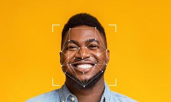 A young man with a cheerful smile is captured against a vibrant yellow background. Facial recognition markers overlay his face, highlighting the technology's application in identification. photo