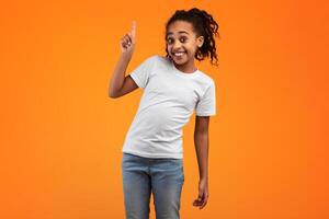 Look There. Portrait Of Smiling African American Girl Pointing With Finger Up Above Her Head, Standing On Orange Yellow Studio Background, Presenting Indicating Your Information. Number One Sign photo