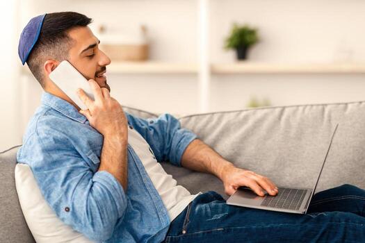 hogar oficina concepto. lado ver perfil retrato de sonriente milenario hombre hablando en inteligente teléfono utilizando ordenador personal a lugar de trabajo, sentado en sofá. joven masculino empleado consultante cliente, chateando con amigos foto