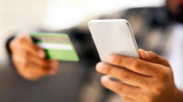 Cropped of man holding cellphone and credit card, banking online or making order on Internet. Unrecognizable middle-eastern guy customer purchasing something, using mobile phone, copy space photo