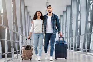 Ready For Vacation. Romantic Middle Eastern Couple Walking With Suitcases At Airport Terminal, Happy Arab Spouses Embracing While Going To Boarding Gate, Enjoying Travelling Together, Copy Space photo
