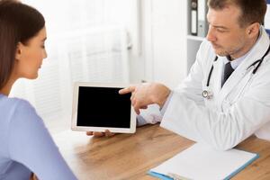 Medical Test And Examination Results. General practitioner showing patient digital tablet with black blank screen, discussing treatment, sitting at the table at office, pointing at monitor photo