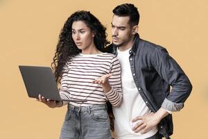 Portrait Of Confused Middle Eastern Couple Suffering Problems With Laptop, Frustrated Young Arab Couple Looking At Computer Screen, Standing Isolated Over Yellow Studio Background, Copy Space photo