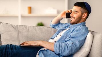 Remote Business. Side Profile View Of Male Freelancer Talking On Cellphone And Working On Laptop At Home Office, Man Using Computer And Having Pleasant Phone Conversation, Enjoying Distance Job photo