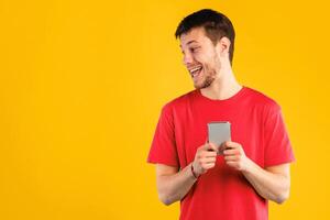 Portrait of positive curious guy holding mobile phone, standing isolated over blue studio background, looking aside, peeking and trying to see something, using device, free space. Man chatting online photo