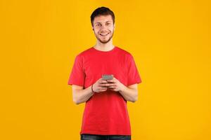 People And Technology Concept. Portrait of happy smiling young man using smartphone standing isolated over blue studio background, copy space. Guy chatting online, looking at camera photo