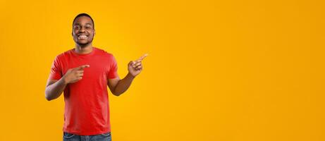 Look There. Cheerful African American Man Pointing Fingers Aside Showing Empty Space For Text Posing Smiling To Camera Over Yellow Background In Studio. Panorama photo