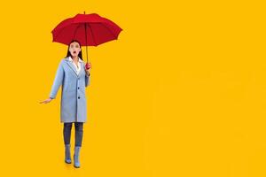 Rainy Weather. Full length of amazed female model standing with open mouth under yellow umbrella at studio photo
