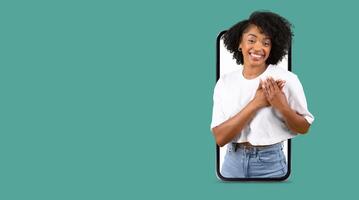A person with curly hair smiles warmly while interacting with a smartphone. The large screen shows a friendly communication moment. The background is isolated with a solid color. photo