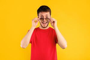 Wow. Portrait of man posing at studio, taking off sunglasses, looking at camera in amazement and with surprised facial expression isolated on blue background. It's Unbelievable. Summer Sale photo