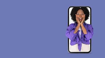 A person with curly hair expresses joy and surprise while looking at a smartphone with a big screen. This moment captures communication and online interaction. photo