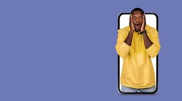 A person in a yellow hoodie shows surprise and joy while using a smartphone with a large screen. The background is a solid color, emphasizing the expression of excitement and the technology in hand. photo