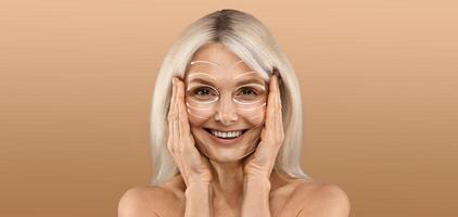A woman with long light hair is smiling and gently applying skincare products on her face. She seems relaxed and happy, surrounded by a serene, empty space that accentuates her beauty routine. photo