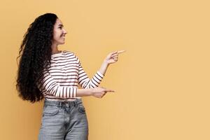 Place For Ad. Cheerful Arab Man And Woman Pointing At Copy Space In The Middle, Happy Middle Eastern Couple Recommending Something While Standing Over Yellow Studio Background, Full Length, Panorama photo