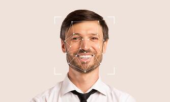 A smiling man is shown with facial recognition markers overlaid. This technology is used for identification and verification. The background provides empty space enhancing focus on the subject. photo