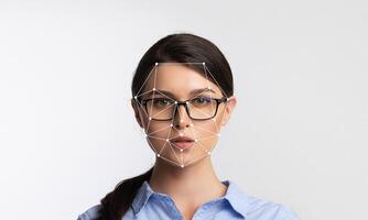 A woman with glasses poses against a light background while facial recognition technology analyzes her features. The focus is on the facial mapping system highlighting key points. photo