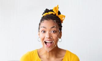 A young woman with a yellow bow in her hair shows a joyful expression while facial recognition technology highlights key features on her face. The background is plain and unobtrusive. photo
