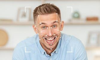 A man with a cheerful expression is interacting with facial recognition technology at his home. The background features a modern decor, enhancing the atmosphere of innovation and engagement. photo