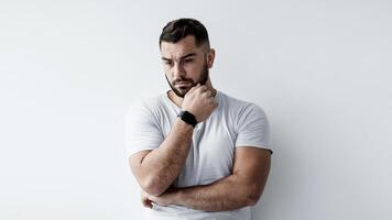 Think, solve problem, negative human emotions, stress and depression. Sad unhappy pensive young european handsome man presses hand to chin and ponders on white wall background, empty space, mockup photo