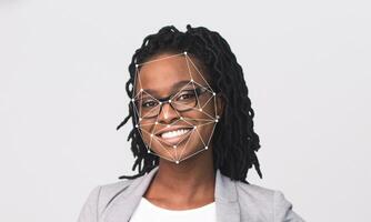 A woman with glasses and dreadlocks smiles at the camera. Facial recognition technology is used to identify distinct facial features against an empty background, emphasizing her expression. photo