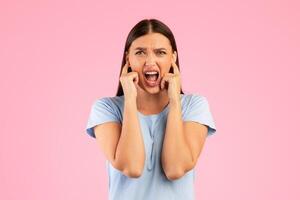 Too loud. Portrait of young annoyed woman closing her ears with fingers, refusing to listen or to hear something, standing isolated over yellow studio background. Lady screaming and shouting photo