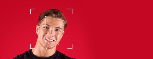 A person smiles while facial recognition technology analyzes their face against a blank red background. This demonstrates the advancements in identification processes in modern society. photo