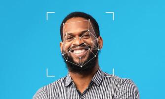 A man smiles confidently against a blue background as facial recognition technology analyzes his features. This highlights advancements in identification processes and their growing presence. photo