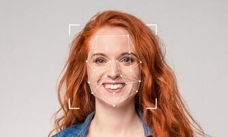 A woman with vibrant red hair is smiling warmly. Her facial features are being analyzed using advanced recognition technology marked with geometric shapes, emphasizing identification. photo