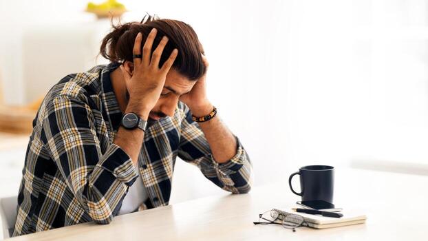 Deprimido árabe hombre sentado a mesa de trabajo con ordenador portátil en oficina, conmovedor su cabeza, sufrimiento desde agotamiento o financiero crisis, joven Medio este empresario teniendo problemas a trabajo, Copiar espacio foto