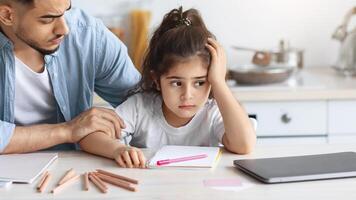 Young arab man single father comforting his upset little daughter, sitting at table with colorful pencils and notebook at kitchen, bored girl kid with unhappy face expression looking at copy space photo