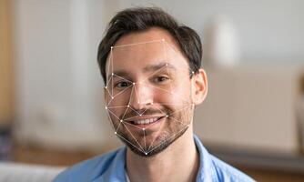 A man sitting in a modern environment smiles as facial recognition technology analyzes his features. The background is blurred, highlighting the focus on facial identification. photo